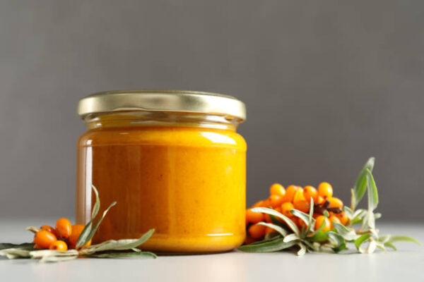 Delicious sea buckthorn jam and fresh berries on grey table. space for text